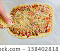 Process of making homemade pizza top view with person hand adding ingredients on raw dough with ham vegetables and cheese on baking sheet domestic kitchen cooking hobby handmade meal preparation 138402818