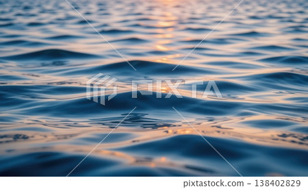 Macro shot of gentle blue sea ripples with golden sunlight reflecting on the water surface at dusk. 138402829
