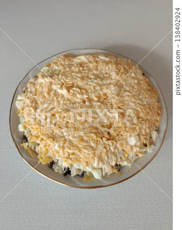 Layered mimosa salad presented on a classic plate, featuring grated cheese, mayonnaise, and eggs, a traditional festive appetizer for celebrations and holiday meals Layered mimosa salad presented on a classic plate, featuring grated cheese, mayonnaise, and eggs, a traditional festive appetizer for celebrations and holiday meals 138402924
