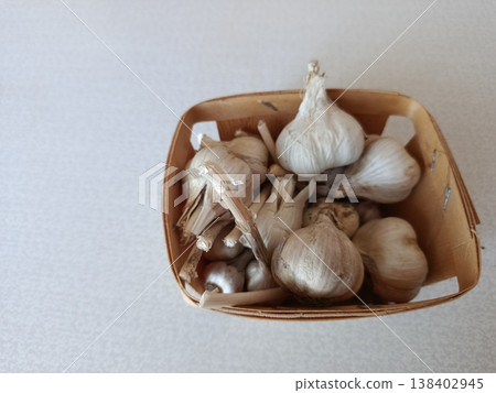 Organic garlic bulbs unpeeled in a small rustic wooden basket, fresh farm-to-kitchen produce for healthy cooking, minimal still life on a light background 138402945