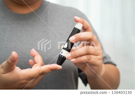 Asian woman self testing to check blood sugar level diabetes by digital lancet on finger at home. 138403130