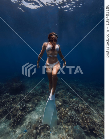 Young slim woman freediving above coral reef in deep blue ocean 138403186