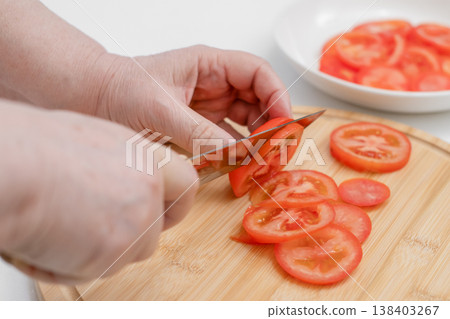 Slicing fresh tomatoes on a wooden cutting board, close-up of food preparation in the kitchen 138403267