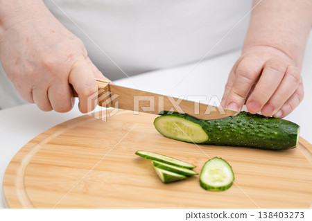 Slicing fresh cucumber on a wooden cutting board, close-up of food preparation in the kitchen Slicing fresh cucumber on a wooden cutting board, close-up of food preparation in the kitchen 138403273