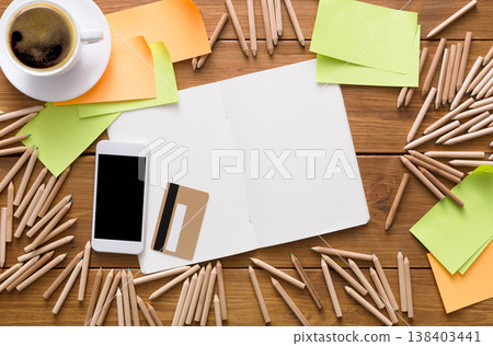Buy stationery online. Flat lay top view shot of workplace of designer or artist with credit card, lots of pencils, mobile phone, sketchbook, sticky memo notes and cup of morning coffee on wooden desk 138403441