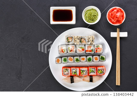 Traditional japanese food restaurant. Colorful sushi set served on white platter with chopsticks, soy sauce, ginger and wasabi. Top view on gray background with copy space 138403442