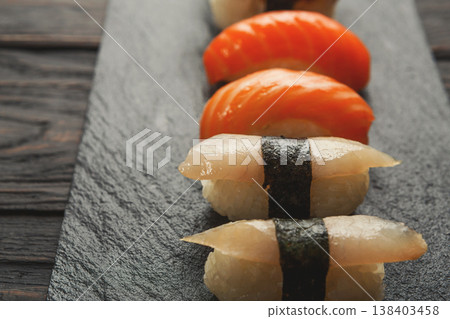 Sushi plate. Japanese food restaurant, eel, salmon and snapper sushi closeup on dark background. Pov with copy space on black wood Sushi plate. Japanese food restaurant, eel, salmon and snapper sushi closeup on dark background. Pov with copy space on black wood 138403458