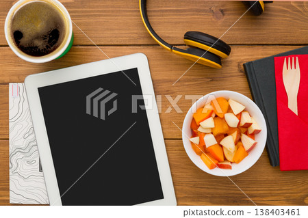 Healthy lunch at workplace with copy space on tablet pc. Top view flat lay of desktop fruit salad in foil container and mobile phone on wooden desk background Healthy lunch at workplace with copy space on tablet pc. Top view flat lay of desktop fruit salad in foil container and mobile phone on wooden desk background 138403461
