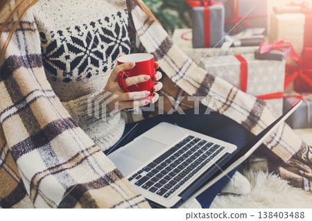 Christmas online shopping. Woman has coffee, buy presents on laptop, prepare to xmas, among gift boxes and packages. Winter sales Christmas online shopping. Woman has coffee, buy presents on laptop, prepare to xmas, among gift boxes and packages. Winter sales 138403488