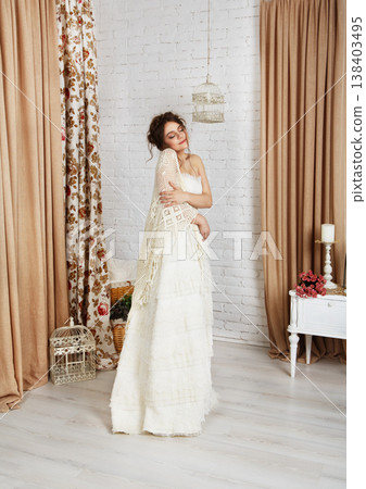 Wedding dress fashion. Beautiful young bride in vintage wedding dress indoors. White wedding dress at model. Girl shows wedding fashion in decorated shabby chic interior with flowers, high key. Wedding dress fashion. Beautiful young bride in vintage wedding dress indoors. White wedding dress at model. Girl shows wedding fashion in decorated shabby chic interior with flowers, high key. 138403495