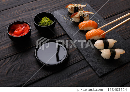 Eating sushi. Japanese food restaurant, unagi and salmon sushi on dark background. Taking piece with chopsticks. Closeup on black wood Eating sushi. Japanese food restaurant, unagi and salmon sushi on dark background. Taking piece with chopsticks. Closeup on black wood 138403524