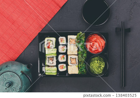 Colorful sushi and rolls platter in japanese restaurant, with teapot and chopsticks top view, copy space on mat Colorful sushi and rolls platter in japanese restaurant, with teapot and chopsticks top view, copy space on mat 138403525