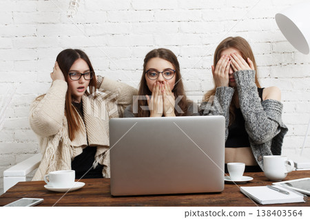 Three friends gather around a laptop in a cafe. They show expressions of surprise and disbelief while drinking coffee. The moment captures their shared experience and reactions. Three friends gather around a laptop in a cafe. They show expressions of surprise and disbelief while drinking coffee. The moment captures their shared experience and reactions. 138403564