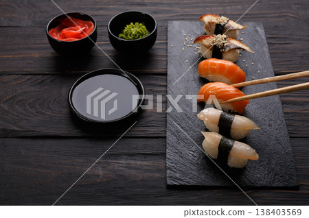 Eating sushi. Japanese food restaurant, unagi and salmon sushi on dark background. Taking piece with chopsticks. Closeup on black wood Eating sushi. Japanese food restaurant, unagi and salmon sushi on dark background. Taking piece with chopsticks. Closeup on black wood 138403569