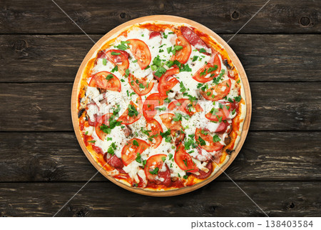 Delicious pizza with mushrooms, tomatoes and chicken ham - thin pastry crust at wooden round desk and rustic wood background. Italian food. Top view Delicious pizza with mushrooms, tomatoes and chicken ham - thin pastry crust at wooden round desk and rustic wood background. Italian food. Top view 138403584