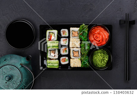 Japanese restaurant delivery, take away box top view, sushi maki and roll set. Chopsticks, ginger, soy sauce, wasabi. Meals at black background Japanese restaurant delivery, take away box top view, sushi maki and roll set. Chopsticks, ginger, soy sauce, wasabi. Meals at black background 138403632