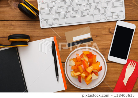 Healthy business lunch at workplace. Top view flat lay of desktop - laptop, notepad, credit card and phone on wooden desk background with plate of fruit salad snack, nobody, objects Healthy business lunch at workplace. Top view flat lay of desktop - laptop, notepad, credit card and phone on wooden desk background with plate of fruit salad snack, nobody, objects 138403633