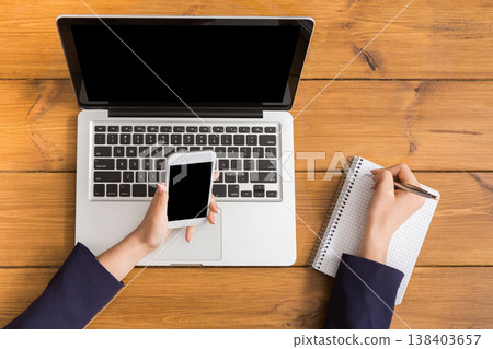 Top view table of business woman checking schedule with mobile phone. Freelancer working with portable computer while sitting at wooden desk at coffee shop Top view table of business woman checking schedule with mobile phone. Freelancer working with portable computer while sitting at wooden desk at coffee shop 138403657