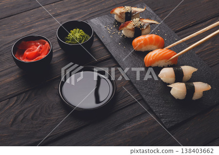 Eating sushi. Japanese food restaurant, unagi and salmon sushi on dark background. Taking piece with chopsticks. Closeup on black wood Eating sushi. Japanese food restaurant, unagi and salmon sushi on dark background. Taking piece with chopsticks. Closeup on black wood 138403662