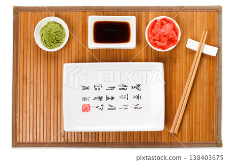 Set of sushi tablewear. Top view on empty rectangular sushi plate with hieroglyphs, saucer, ginger, wasabi and chopsticks on bamboo mat. Flat lay, copy space, background Set of sushi tablewear. Top view on empty rectangular sushi plate with hieroglyphs, saucer, ginger, wasabi and chopsticks on bamboo mat. Flat lay, copy space, background 138403675