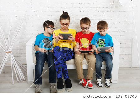 Group of kids in eye glasses look into their phones and tablets. Children computer games, social networks and media addiction concept. Girl and boys with tablet and smartphones. Communication problems 138403709