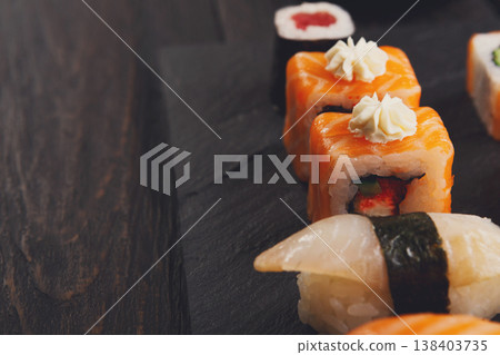 Sushi plate. Japanese food restaurant, unagi and salmon rolls closeup on dark background. Pov with copy space on black wood Sushi plate. Japanese food restaurant, unagi and salmon rolls closeup on dark background. Pov with copy space on black wood 138403735