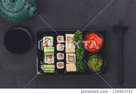 Japanese restaurant delivery, take away box top view, sushi maki and roll set. Chopsticks, ginger, soy sauce, wasabi and teapot. Meals at black background Japanese restaurant delivery, take away box top view, sushi maki and roll set. Chopsticks, ginger, soy sauce, wasabi and teapot. Meals at black background 138403747