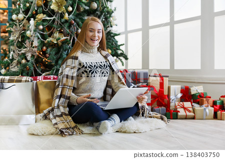 Happy girl with laptop sitting at decorated christmas tree background. Woman got greeting email from online shop with huge discount at winter sale. Holiday atmosphere, copy space Happy girl with laptop sitting at decorated christmas tree background. Woman got greeting email from online shop with huge discount at winter sale. Holiday atmosphere, copy space 138403750