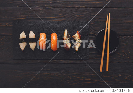 Sushi plate. Japanese food restaurant, unagi and salmon sushi on dark background. Set with chopsticks and soy sauce. Top view on black wood 138403766