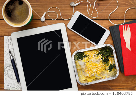 Healthy business lunch at workplace. Top view flat lay of desktop - tablet pc with copy space and phone on wooden desk background with snack in foil container 138403795