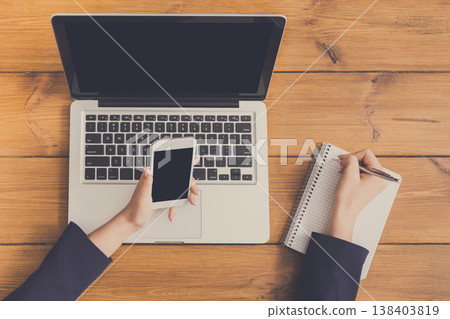 Top view table of business woman checking schedule with mobile phone. Freelancer working with portable computer while sitting at wooden desk at coffee shop Top view table of business woman checking schedule with mobile phone. Freelancer working with portable computer while sitting at wooden desk at coffee shop 138403819