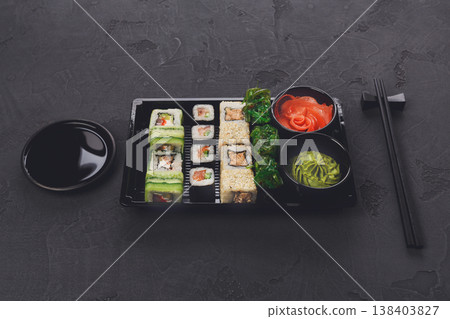 Japanese restaurant delivery, take away box top view, sushi maki and roll set. Chopsticks, ginger, soy sauce, wasabi. Meals at black background 138403827