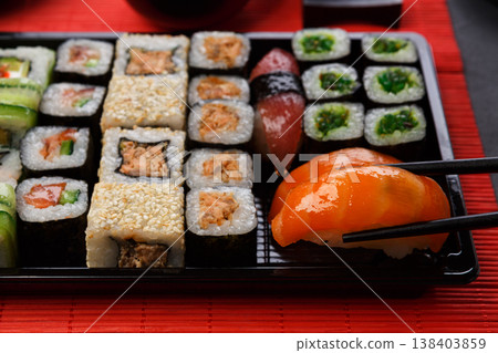 Eating salmon sushi. Japanese food restaurant, sushi maki and roll plate or platter set. Closeup of hand with chopsticks taking roll. 138403859