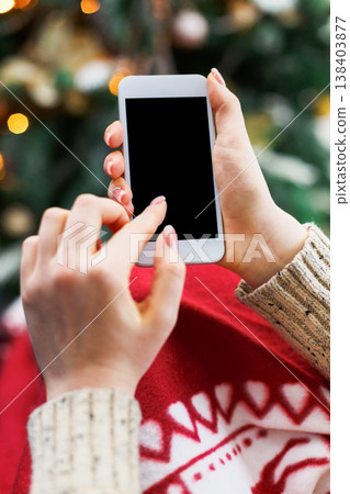Christmas online shopping. Female buyer makes order at screen of smartphone with copy space. Woman buys presents for xmas eve, sits at home near decorated xmas tree. Winter holidays sales 138403877