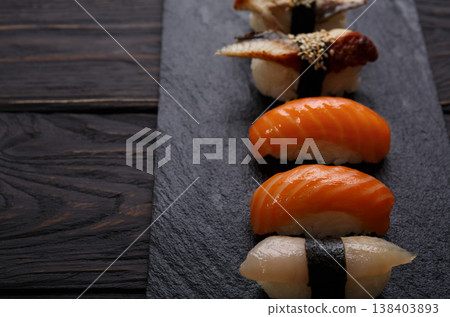 Sushi plate. Japanese food restaurant, eel, salmon and snapper sushi closeup on dark background. Pov with copy space on black wood Sushi plate. Japanese food restaurant, eel, salmon and snapper sushi closeup on dark background. Pov with copy space on black wood 138403893