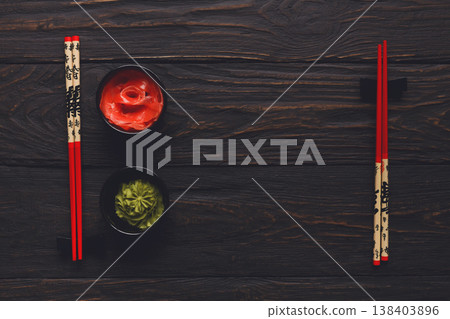 Pieces of traditional japanese tablewear. Red chopsticks with hierogliphs, small black bowls with ginger and wasabi on dark wooden table. Top view, flat lay, copy space, background Pieces of traditional japanese tablewear. Red chopsticks with hierogliphs, small black bowls with ginger and wasabi on dark wooden table. Top view, flat lay, copy space, background 138403896