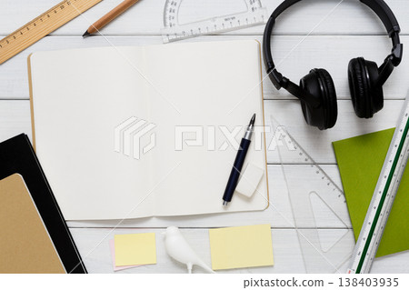 Education and work concept, top view shot of workplace. Stationery supplies - blank notepad, pen, binder clips, ruler, paperclips and headphones on white wooden desktop, flat lay, copy space, mockup Education and work concept, top view shot of workplace. Stationery supplies - blank notepad, pen, binder clips, ruler, paperclips and headphones on white wooden desktop, flat lay, copy space, mockup 138403935
