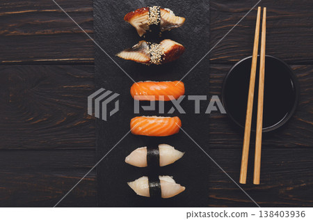 Sushi plate. Japanese food restaurant, unagi and salmon sushi on dark background. Set with chopsticks and soy sauce. Top view on black wood Sushi plate. Japanese food restaurant, unagi and salmon sushi on dark background. Set with chopsticks and soy sauce. Top view on black wood 138403936