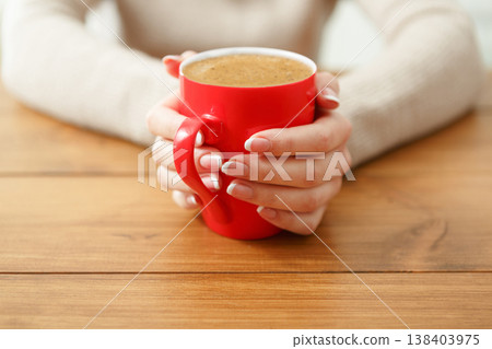 Woman holding a cup of hot drink while sitting at wooden table, shallow depth of field. Woman holding a cup of hot drink while sitting at wooden table, shallow depth of field. 138403975