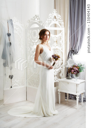 Wedding dress fashion. Beautiful young bride in vintage wedding dress indoors. White wedding dress at model. Girl shows wedding fashion in decorated shabby chic interior with flowers, high key. Wedding dress fashion. Beautiful young bride in vintage wedding dress indoors. White wedding dress at model. Girl shows wedding fashion in decorated shabby chic interior with flowers, high key. 138404143