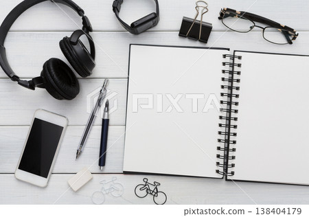 Modern office background. Stationery, open notepad, smart watch, headhphones, glasses and mobile on white wooden table. Top view on stylish workspace with copy space on blank textbook Modern office background. Stationery, open notepad, smart watch, headhphones, glasses and mobile on white wooden table. Top view on stylish workspace with copy space on blank textbook 138404179