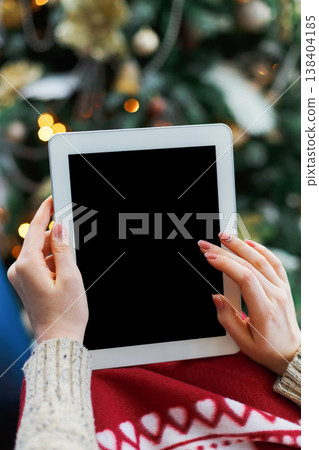 Christmas online shopping. Female buyer makes order at screen of tablet with copy space. Woman buys presents prepare to xmas eve, sits at home near decorated xmas tree. Winter holidays sales Christmas online shopping. Female buyer makes order at screen of tablet with copy space. Woman buys presents prepare to xmas eve, sits at home near decorated xmas tree. Winter holidays sales 138404185