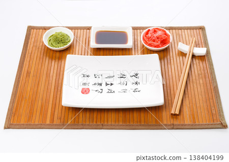 Set of sushi tablewear. Empty rectangular sushi plate with hieroglyphs, saucer, ginger, wasabi and chopsticks on bamboo mat. Flat lay, copy space, background 138404199