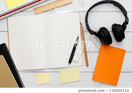 Education and work concept, top view shot of workplace. Stationery supplies - blank notepad, pen, binder clips, ruler, paperclips and headphones on white wooden desktop, flat lay, copy space, mockup Education and work concept, top view shot of workplace. Stationery supplies - blank notepad, pen, binder clips, ruler, paperclips and headphones on white wooden desktop, flat lay, copy space, mockup 138404210