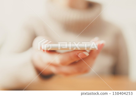 Female holding smartphone while sitting at wooden table, selective focus, close up. 138404253