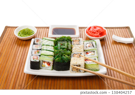 Japanese food restaurant background. Sushi maki, gunkan and rolls platter set served on bamboo mat with soy sauce, ginger, wasabi and chopstiks taking one piece, pov, copy space 138404257