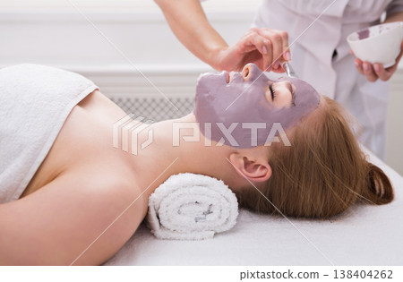 Apply clay face mask, spa beauty treatment and skincare. Woman getting facial nourishing mask by beautician at spa salon, close-up Apply clay face mask, spa beauty treatment and skincare. Woman getting facial nourishing mask by beautician at spa salon, close-up 138404262