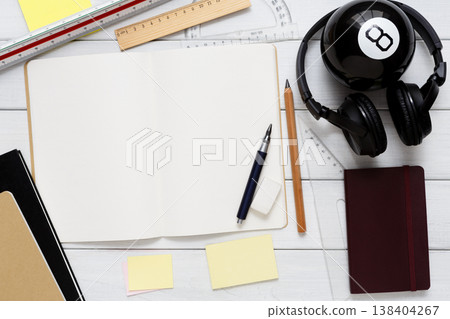 Education and work concept, top view shot of workplace. Stationery supplies - blank notepad, pen, binder clips, ruler, paperclips and headphones on white wooden desktop, flat lay, copy space, mockup 138404267