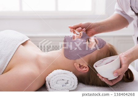 Apply clay face mask, spa beauty treatment and skincare. Woman getting facial nourishing mask by beautician at spa salon, close-up 138404268