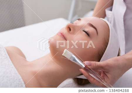 Apply face mask, spa beauty treatment and skincare. Woman getting facial nourishing mask by beautician at spa salon, close-up Apply face mask, spa beauty treatment and skincare. Woman getting facial nourishing mask by beautician at spa salon, close-up 138404288